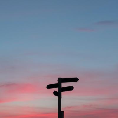 panneaux pointant des directions différents devant un coucher de soleil. 