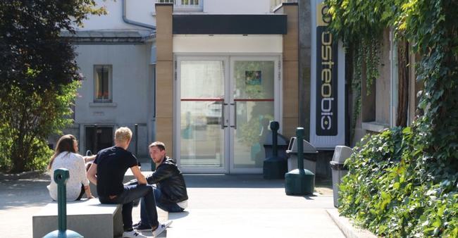 Photo porte d'entrée de l'école d'ostéopathie Ostéobio Paris avec 3 élèves assis devant